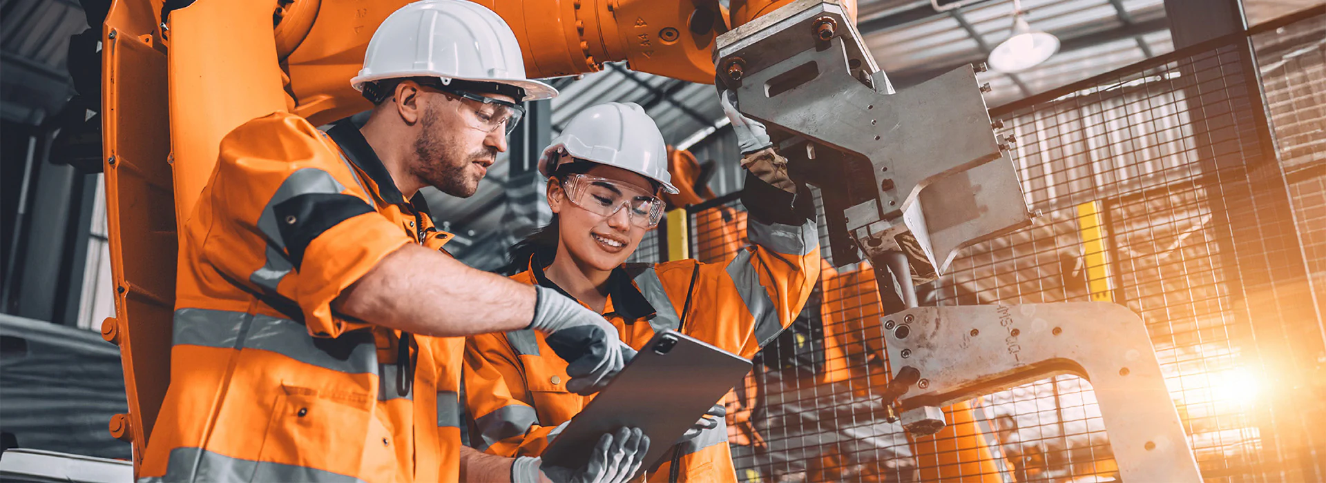Bildbeschreibung / description: Zwei Arbeiter in orangefarbener Schutzausrüstung schauen in einer Fabrik auf ein Tablet.