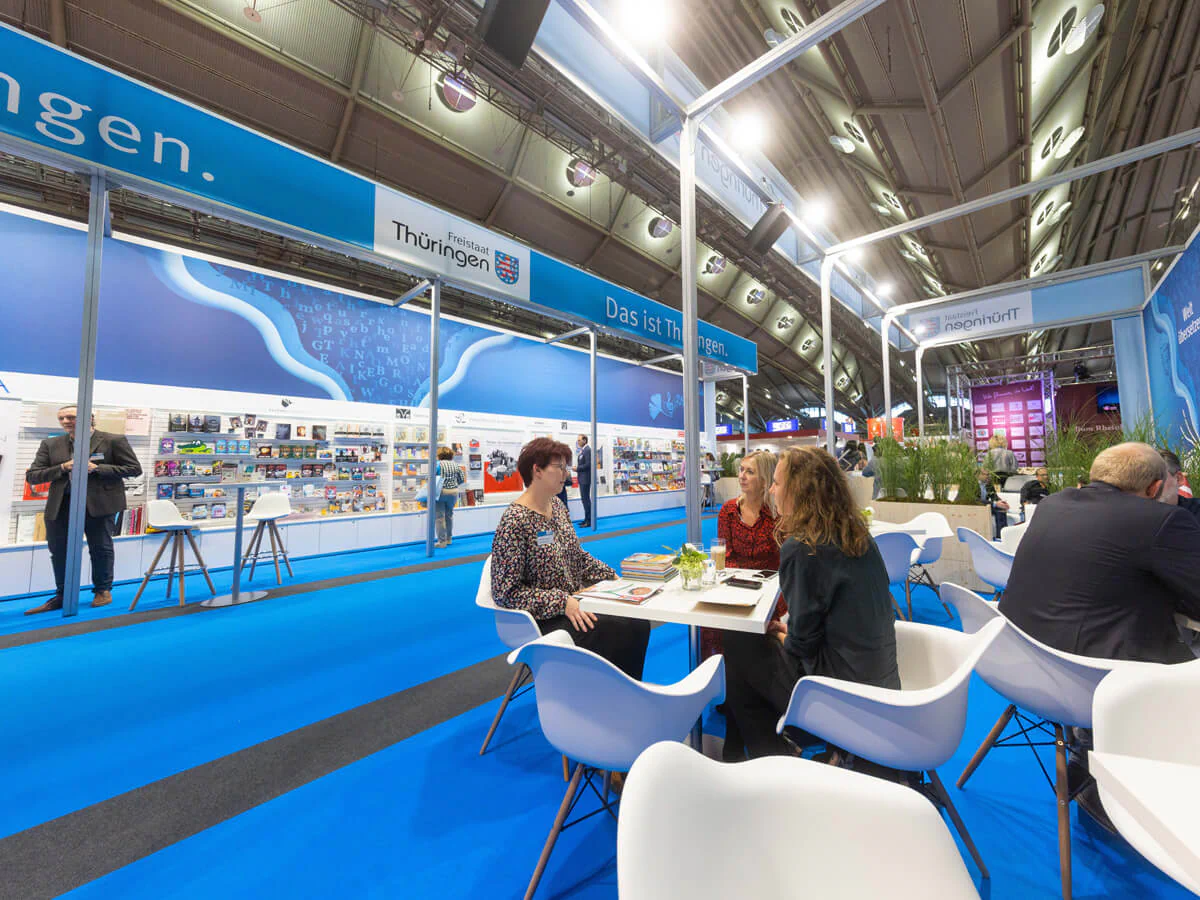 Bildbeschreibung / description: Menschen sitzen an einem Messestand und unterhalten sich